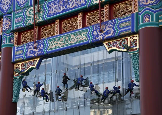 Window cleaners work on the exterior of a building of a state-run bank are seen behind a traditional gateway in  Beijing, China, January 9, 2016. (Photo by Kim Kyung-Hoon/Reuters)