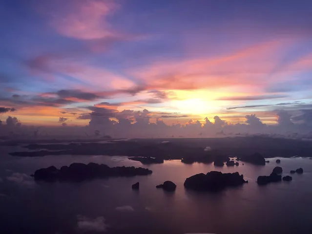 The sun sets over outlying islands as a plane prepares to land on the resort island of Phuket, Thailand on Wednesday, May 22, 2019. Thailand hopes to first fully reopen the island of Phuket, its most popular destination, by July 1 for vaccinated visitors without quarantine. But they will be required to spend a certain time, possibly up to a week, on Phuket before they are allowed to travel elsewhere in Thailand. (Photo by Adam Schreck/AP Photo)