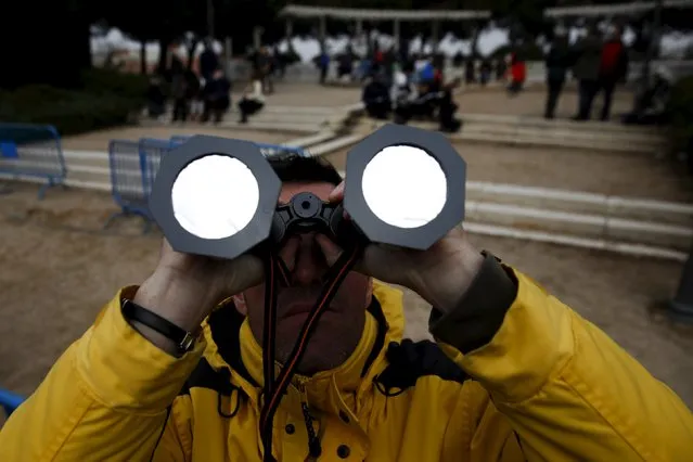 A man uses binoculars with special filters as he watches a partial solar eclipse, despite the cloudy weather, at Madrid's Planetarium March 20, 2015. A solar eclipse swept across the Atlantic Ocean on Friday with the moon set to block out the sun for a few thousand sky gazers on remote islands with millions more in Europe, Africa and Asia getting a partial celestial show. (Photo by Sergio Perez/Reuters)