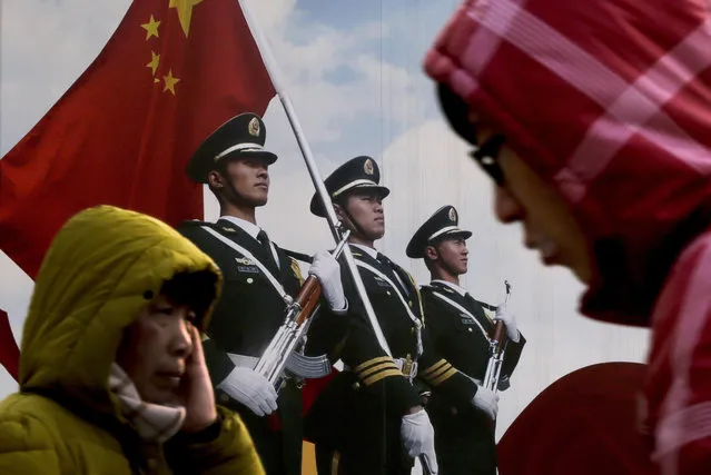 People walk past a poster of Chinese People's Liberation Army (PLA) soldiers on display in Beijing, Thursday, January 21, 2016. China’s armed forces have shut down newspapers published by the country’s seven military regions as part of a program to downsize and streamline the world’s largest standing military. (Photo by Andy Wong/AP Photo)