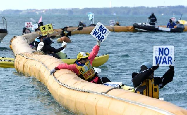 Protesters on canoes display placard as construction workers dumped a truckload of sediment on the ground and bulldozed it into the sea at Henoko on Okinawa’s east coast to build a runway for a Marine Corps base, Friday, December 14, 2018. Japan's central government started main reclamation work Friday at a disputed U.S. military base relocation site on the southern island of Okinawa despite fierce local opposition. (Photo by Koji Harada/Kyodo News via AP Photo)