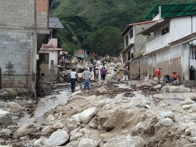 People walk on the street covered in mud following flash flooding in Tovar, Merida State, Venezuela on August 25, 2021.  (Photo by Courtesy of Comunicacion Continua/comunicacioncontinua.com/Handout via Reuters)