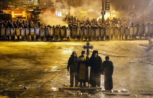 Orthodox priests pray as they stand between pro-European Union activists and police lines in central Kiev, Ukraine, on January 24, 2014. A top opposition leader on Thursday urged protesters to maintain a shaky cease-fire with police after at least two demonstrators were killed in clashes this week, but some in the crowd appeared defiant, jeering and chanting “revolution” and “shame”. (Photo by Sergei Grits/Associated Press)