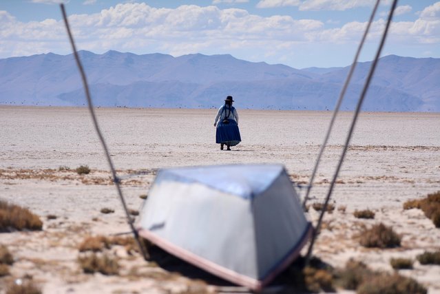 Cristina Mamani walks near an unused boat in Lake Poopo, Bolivia's second largest lake which has dried up due to water diversion for regional irrigation needs and a warmer, drier climate, according to local residents and scientists, in Lake Poopo, Bolivia on July 24, 2021. (Photo by Claudia Morales/Reuters)
