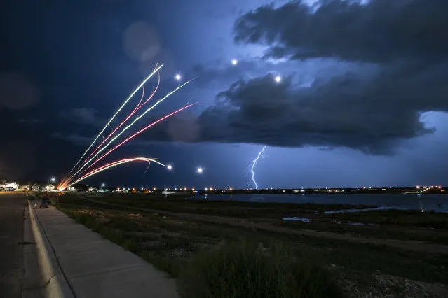 Bobby Florez lights fireworks with his nephew Kaden Perez, 5, as a lightning storm passes by in the distance Friday night, July 2, 2021, in Odessa, Texas. Flores and his family began their celebrations two nights before Independence Day. (Photo by Eli Hartman/Odessa American via AP Photo)