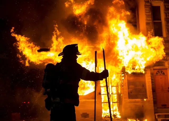 A Baltimore firefighter attacks a fire at a convenience store and residence during clashes after the funeral of Freddie Gray in Baltimore, Maryland in the early morning hours of April 28, 2015. (Photo by Eric Thayer/Reuters)