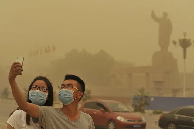 A couple wears facemarks as they pose for a self-portrait near a large statue of late Chinese leader Mao Zedong during a sandstorm in Kashgar city in northwestern China's Xinjiang Uighur Autonomous Region, Sunday May 10, 2015. (Photo by Chinatopix via AP Photo)