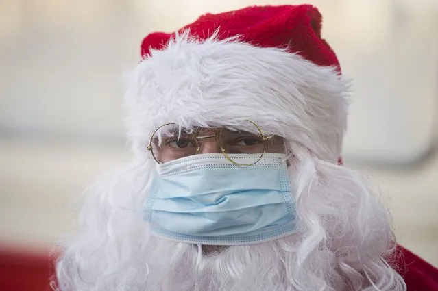 A person wearing a Santa Claus outfit and a mask for protection against the COVID-19 infection stands, during a Christmas event organized by the public transport company in Romania's capital n Bucharest, Romania, Sunday, December 19, 2021. (Photo by Alexandru Dobre/AP Photo)