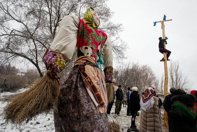 A man climbs up a wooden pole to get a prize next to an effigy of Lady Maslenitsa during celebrations of Maslenitsa, also known as Pancake Week, which is a pagan holiday marking the end of winter, in the village of Sokuluk, Kyrgyzstan, March 14, 2021. (Photo by Vladimir Pirogov/Reuters)