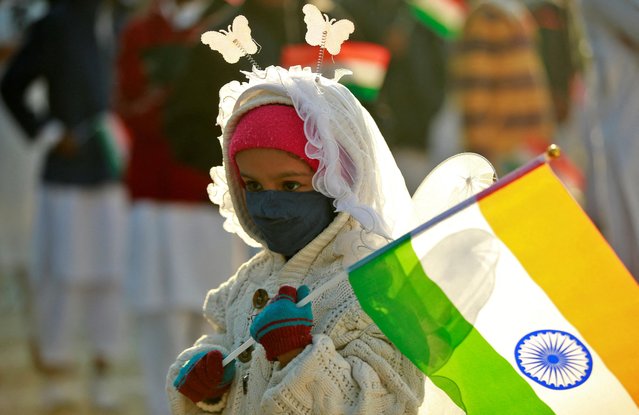 A girl wearing a face mask holds the Indian national flag as she attends a flag hoisting ceremony during India's Republic Day celebrations in Ahmedabad, India, January 26, 2022. (Photo by Amit Dave/Reuters)