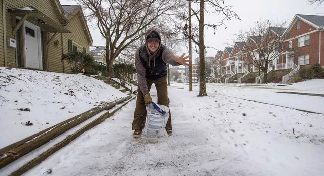Austin Wilder tosses salt on sidewalks for their properties in Bloomington, Ind., on Thursday, February 3, 2022. A major winter storm with millions of Americans in its path is spreading rain, freezing rain and heavy snow further across the country. (Photo by Rich Janzaruk/The Herald-Times via AP Photo)