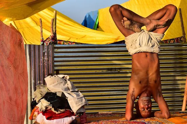 An ascetic performs yoga at his makeshift tent near the banks of Sangam -the confluence of the Ganges, Yamuna and mythical Saraswati river during the Magh Mela festival in Allahabad on January 28, 2022. (Photo by Sanjay Kanojia/AFP Photo)