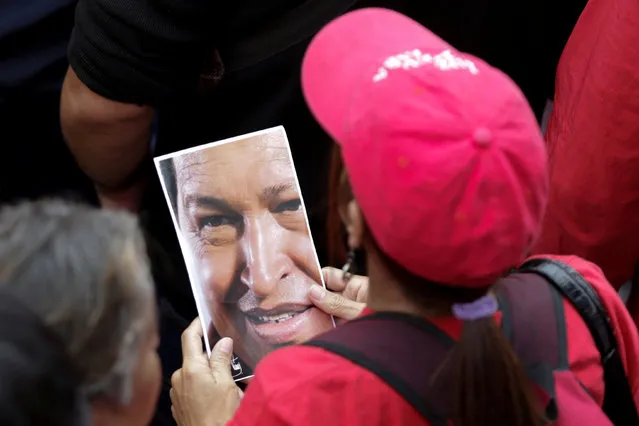 A supporter of Venezuela's President Nicolas Maduro holds a portrait of Venezuela's late President Hugo Chavez, during a rally to commemorate May Day, in Caracas, Venezuela, May 1, 2016. (Photo by Marco Bello/Reuters)