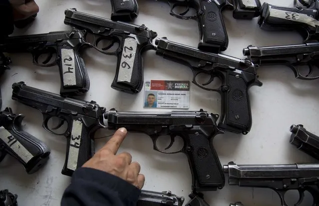 A federal police looks for the assigned weapon that corresponds to the rural police's identification card before the start of a ceremony in Tepalcatepec, Mexico, Saturday, May 10, 2014. At the ceremony in the town where the vigilante movement began in February 2013, officials handed out new pistols, rifles and uniforms to 120 self-defense group members who were sworn into a new official rural police force. (Photo by Eduardo Verdugo/AP Photo)