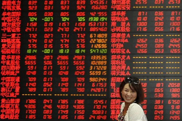 An investor smiles as she walks past an electronic board showing stock information at a brokerage house in Fuyang, Anhui province, China, July 17, 2015. China stocks closed up on Friday, overcoming a mid-week slide to end up for a second week, with market insiders saying the “national team” of brokerages, mutual funds and market regulators were intensifying intervention, especially in the futures market. (Photo by Reuters/Stringer)