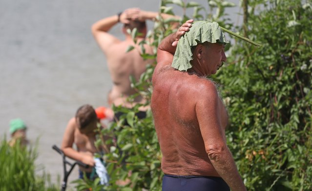 A man covers his head with a leaf during a hot day at a pond at residential district in Moscow, Russia, 03 July 2024. The temperatures in Moscow exceeded 33 degrees Celsius. (Photo by Maxim Shipenkov/EPA/EFE)