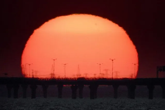 The sun sets behind the Sheikh Jaber Causeway in Kuwait City on February 6, 2022. (Photo by Yasser Al-Zayyat/AFP Photo)