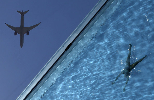 A person swims during hot weather at the Embassy Gardens Sky Pool, a transparent acrylic swimming pool suspended between two buildings, as an aircraft flies overhead, in London, Britain, on July 19, 2024. (Photo by Toby Melville/Reuters)