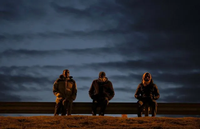 Migrants sit by a roadside as darkness falls, near to the Eurotunnel site in Calais, France, August 4, 2015. Many migrants, each night, wait for darkness prior to heading for the Channel tunnel entrance, where they attempt to illegally jump onto moving freight trains bound for Britain. (Photo by Peter Nicholls/Reuters)