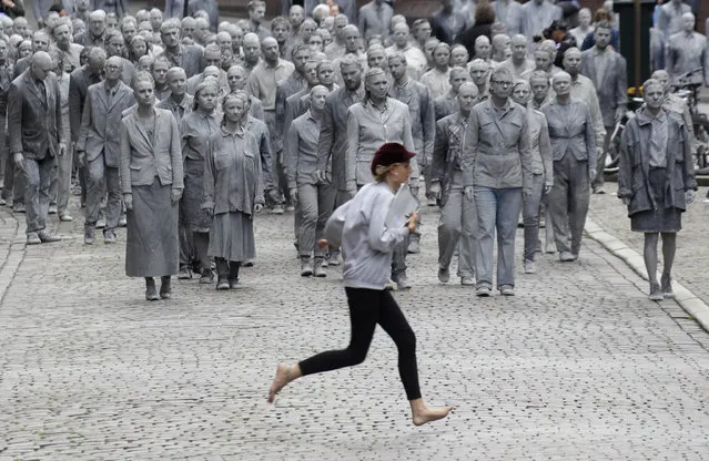A woman crosses the street in front of the approaching performance “1000 Gestalten” with hundreds of people painted like clay figures moving slowly and silently through the streets of Hamburg to protest against the G-20 summit in Hamburg, northern Germany, Wednesday, July 5, 2017. (Photo by Matthias Schrader/AP Photo)