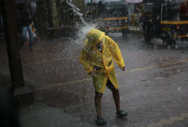 A boy stands beneath water poring from a roof during monsoon rains in Mumbai, India, Monday, July 7, 2014.The monsoon rains usually hit India from June to September. (Photo by Rafiq Maqbool/AP Photo)