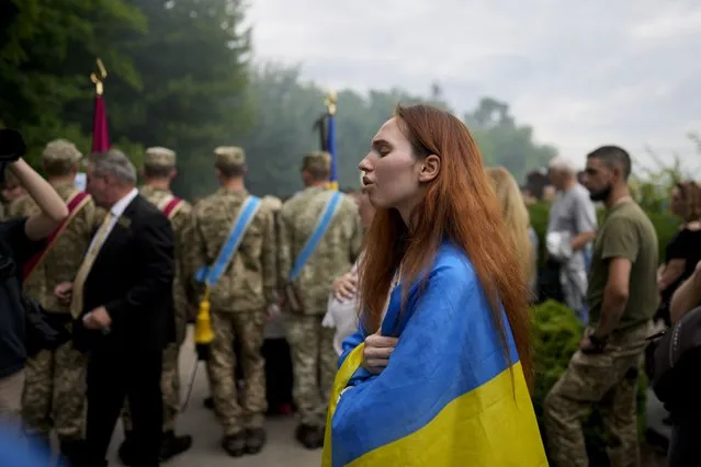 A woman wrapped in a Ukrainian flag attends the funeral of activist and soldier Roman Ratushnyi in Kyiv, Ukraine, Saturday, June 18, 2022. Ratushnyi died in a battle near Izyum, where Russian and Ukrainian troops are fighting for control of the area. (Photo by Natacha Pisarenko/AP Photo)
