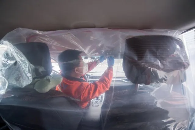 A worker installs plastic film to separate the front seats from the back, inside a vehicle for a car-hailing service in Taiyuan, Shanxi province, China on February 14, 2020. (Photo by Cnsphoto via Reuters)