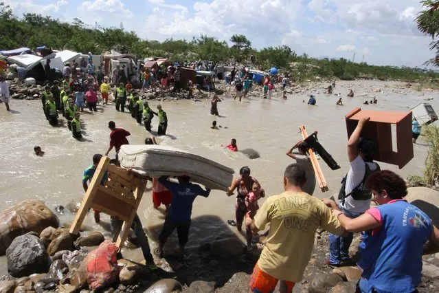 People carry their household belongings across the Tachira River from Venezuela, foreground, to Colombia, near San Antonio del Tachira, Venezuela, Tuesday, August 25, 2015, during a mass exodus of Colombians living on the Venezuelan side of the border. (Photo by Eliecer Mantilla/AP Photo)