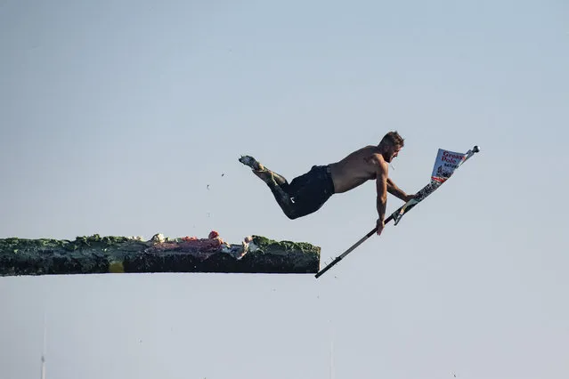 Anthony Novello, 33, grabs the flag and dives off the pole during St. Peter's Fiesta in Gloucester, Massachusetts on June 25, 2022. The festival, and the sports contest, during which contestants try to capture a flag at the end of a slippery pole, haven’t been held since 2019. The contest dates back nearly a century. (Photo by Joseph Prezioso/AFP)