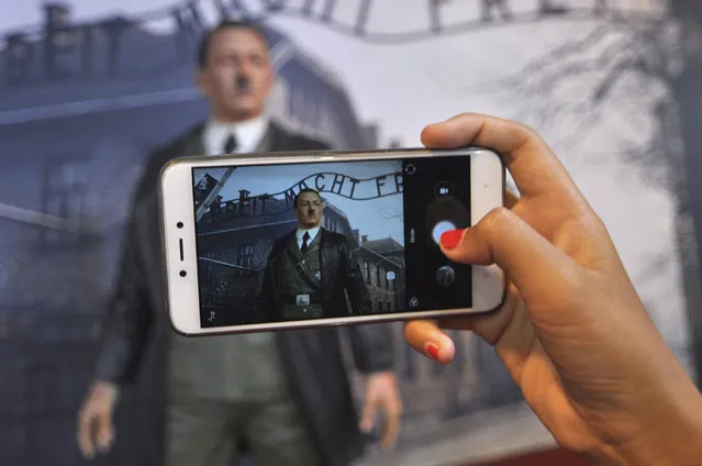 In this Wednesday, November 8, 2017 photo, a visitor uses her mobile phone to take a photo of the wax figure of Adolf Hitler displayed against the backdrop of an image of Nazi Death Camp Auschwitz-Birkenau at De Mata Museum in Yogyakarta, Indonesia. Rights groups have expressed outrage over the display calling it “sickening” and demanded its immediate removal. (Photo by Slamet Riyadi/AP Photo)