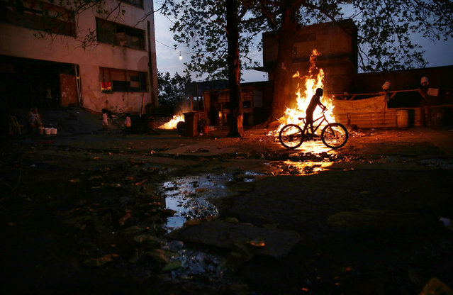 A boy rides a bike past a trash fire outside an occupied building in the Mangueira “favela” community on August 9, 2016 in Rio de Janeiro, Brazil. (Photo by Mario Tama/Getty Images,)