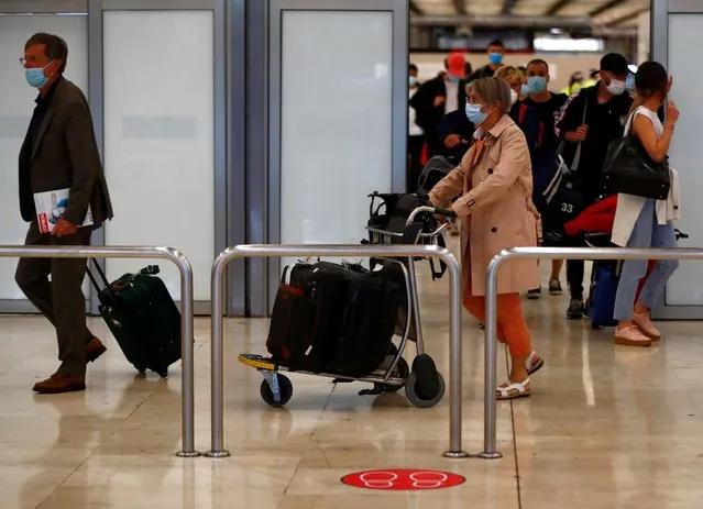 Passengers, wearing protective face masks, walk past a social distancing sign upon arrival from Paris at Adolfo Suarez Barajas airport as Spain reopens its borders to most European visitors after the coronavirus lockdown, in Madrid, Spain, June 21, 2020. (Photo by Sergio Perez/Reuters)