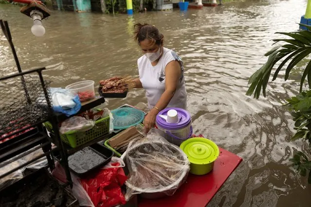 A woman prepares barbecue to sell along a flooded street following heavy rains brought by tropical storm Nalgae, in Imus, Cavite province, Philippines on October 30, 2022. (Photo by Eloisa Lopez/Reuters)