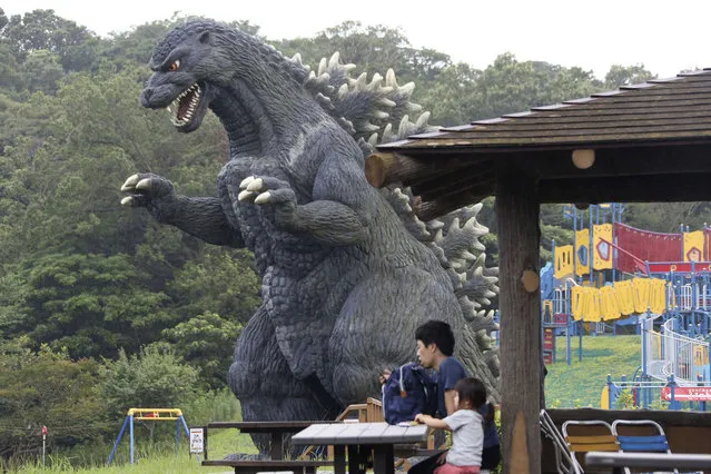 A family sit on a bench near a Godzilla's slide at Kurihama flower park in Yokosuka, near Tokyo Wednesday, July 15, 2020. (Photo by Koji Sasahara/AP Photo)