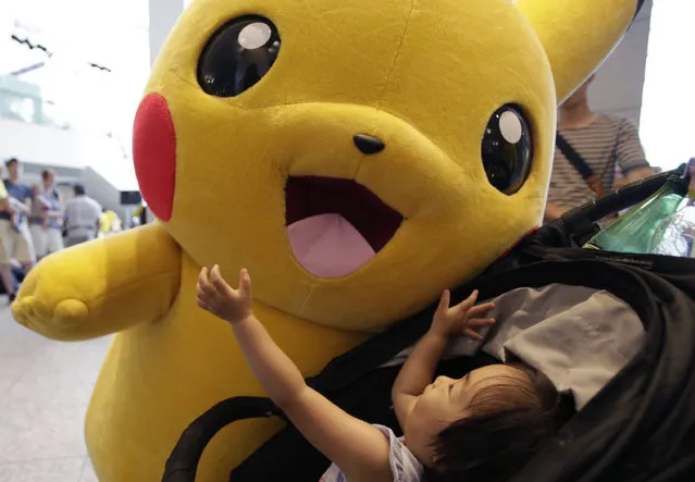 A girl on a baby stroller plays with Pokemon character Pikachu during a special gathering event of Pikachu at Minatomirai shopping district in Yokohama, near Tokyo, Wednesday, August 10, 2016. (Photo by Shizuo Kambayashi/AP Photo)