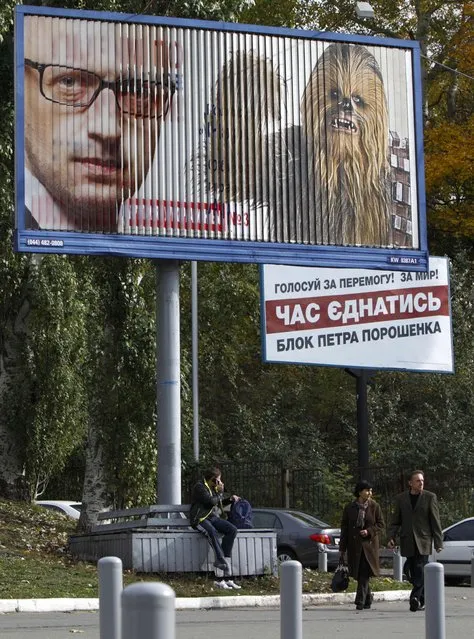 People walk past a pre-election poster with a portrait of Ukraine's Prime Minister Arseny Yatseniuk, leader of political party People's Front, and a candidate from the Internet party of Ukraine, Stepan Chewbacca, in the centre of Kiev October 21, 2014. Ukrainians will take part in an early parliamentary election on October 26. (Photo by Valentyn Ogirenko/Reuters)