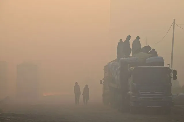 Labourers load goods on a truck along a road amid heavy smog conditions in Lahore on December 1, 2022. (Photo by Arif Ali/AFP Photo)