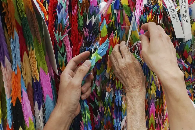 Hatsue Onda, center, is helped by Kengo Onda to offer strings of colorful paper cranes to the victims of the 1945 Atomic bombing near Hiroshima Peace Memorial Museum in Hiroshima, western Japan, Monday, August 3, 2020. The origami cranes that can be seen throughout the city became a symbol of peace because of atomic bomb survivor Sadako Sasaki, who, while battling leukemia, folded similar cranes using medicine wrappers after hearing an old Japanese story that those who fold a thousand cranes are granted one wish. (Photo by Eugene Hoshiko/AP Photo)