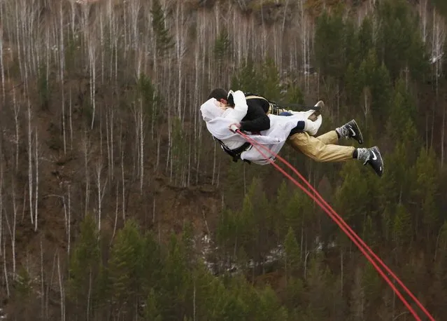 A newly married couple, members of the amateur rope-jumping group “Exit Point”, jumps from a 44-metre high (144-ft) water pipe bridge in the Siberian Taiga area outside Krasnoyarsk, November 2, 2014. Rope-jumping, an extreme sport, involves jumping from a high point using an advanced leverage system combining mountaineering and rope safety equipment. (Photo by Ilya Naymushin/Reuters)