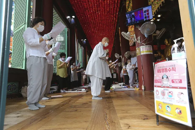 People wearing face masks to help protect against the spread of the coronavirus pray while maintaining social distancing during a service at the Chogyesa temple in Seoul, South Korea, Sunday, August 23, 2020. The sign on a poster reads “Precautions against the coronavirus”. (Photo by Ahn Young-joon/AP Photo)