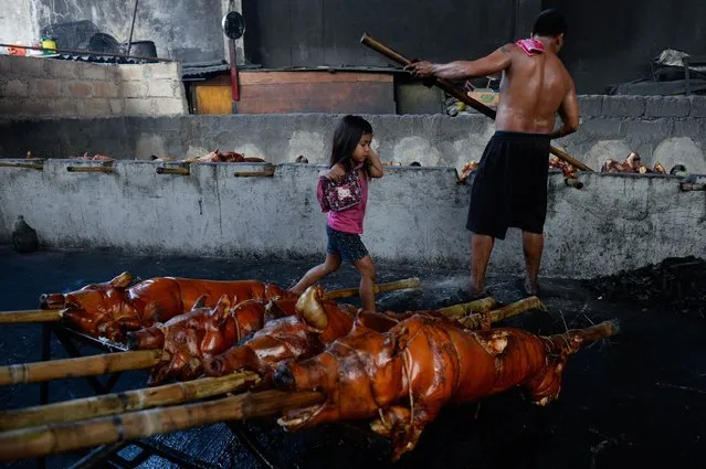 A child skips over bamboo skewered roasted pigs at a “lechon” grill on Christmas Eve in Manila on December 24, 2017. Locally known as “lechon” or roasted suckling pig, the delicacy has been a famous part of Filipino Christmas and New Year celebrations which runs from December until the second week of January. (Photo by George Calvelo/AFP Photo)