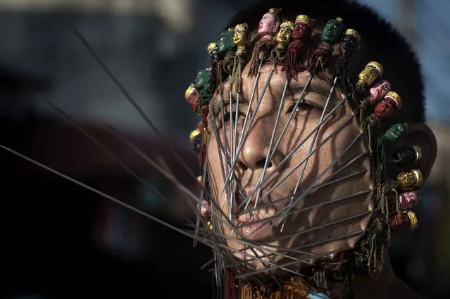 A devotee of the Chinese Jui Tui Shrine has his face pierced with metal rods during a street procession during the annual Vegetarian Festival in the southern Thai town of Phuket on October 19, 2015. During the festival, which begins on the first evening of the ninth lunar month and lasts nine days, religious devotees slash themselves with swords, pierce their cheeks with sharp objects and commit other painful acts to purify themselves, taking on the sins of the community. (Photo by Nicolas Asfouri/AFP Photo)