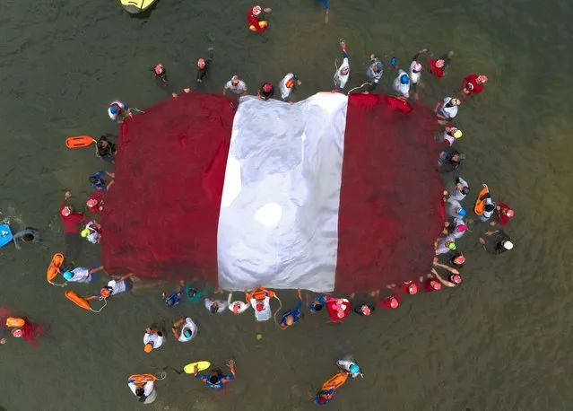 Swimmers, paddlers and surfers form a circle around a Peruvian national flag as a show for unity and peace, in the waters of Agua Dulce beach in Lima, Peru, Saturday, February 4, 2023. Peruvians have found ways to manage their daily lives even as police and protesters clash across the country amid political turmoil over the removal of former President Pedro Castillo who was later arrested for trying to dissolve Congress. (Photo by Guadalupe Pardo/AP Photo)