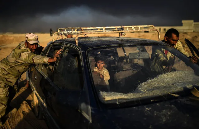 An Iraqi forces member helps a displaced man push a car as they arrive at refugee camp on October 22, 2016 in the town of Qayyarah, south of Mosul, as an operation to recapture the city of Mosul from the Islamic State group takes place. Iraqi security forces battled for a second day with Islamic State group gunmen who infiltrated Kirkuk in a brazen raid that rattled Iraq as it ramped up an offensive to retake Mosul. (Photo by Bulent Kilic/AFP Photo)