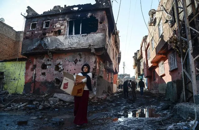 People walk among rubble and damaged buildings in the Sur district in Diyarbakir on December 11, 2015. A policeman was killed on December 9, 2015 by sniper fire as he tried to defuse an explosive device in the Sur district of Diyarbakir province, which has been under military curfew for eight days. Turkey has been waging a relentless offensive against PKK strongholds in the southeast of the country and in northern Iraq following the collapse in July of a two-year truce with rebels. (Photo by Ilyas Akengin/AFP Photo)