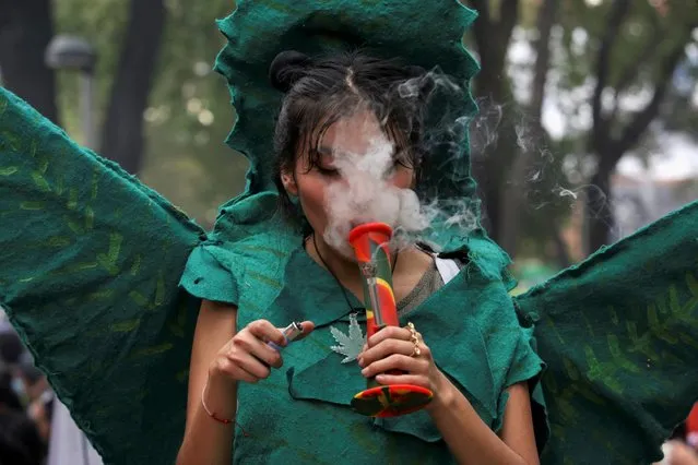 A woman, wearing a custom of a marijuana leaf, smokes marijuana out of a bong during the annual but informal cannabis holiday, 4/20 (four-twenty), corresponding to the numerical figure widely recognized within the cannabis subculture as a symbol for all things related to marijuana, outside the Senate building in Mexico City, Mexico on April 20, 2022. (Photo by Quetzalli Nicte-Ha/Reuters)