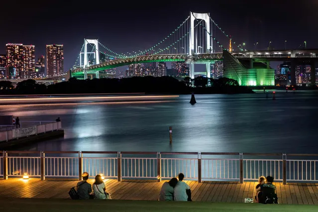 This photo taken on July 1, 2018 shows couples enjoying the night view of Rainbow Bridge along Tokyo Bay. (Photo by Martin Bureau/AFP Photo)