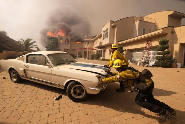 Firefighters push a vehicle from a garage as the Woolsy fire burning a home near Malibu Lake in Malibu, Calif., Friday, November 9, 2018.  About two-thirds of the city of Malibu was ordered evacuated early Friday as a ferocious wildfire roared toward the beachside community that is home to about 13,000 residents, some of them Hollywood celebrities. (Photo by Ringo H.W. Chiu/AP Photo)