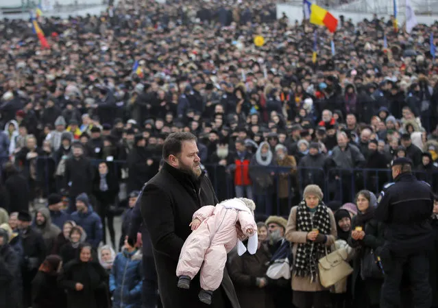 A man carries a baby to receive the Holy Communion during the blessing service of the National Cathedral, in Bucharest, Romania, Sunday, November 25, 2018. Tens of thousands of Romanians gathered for the blessing of a grandiose Orthodox cathedral, also called the “Salvation of the People” cathedral, consecrated to mark 100 years since modern-day Romania was created in the aftermath of World War I. (Photo by Vadim Ghirda/AP Photo)