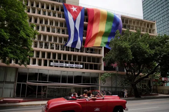 People pass in a vintage car in front of a rainbow flag hanging beside a Cuban flag at the Health Ministry building in Havana, Cuba, May 17, 2021. (Photo by Alexandre Meneghini/Reuters)